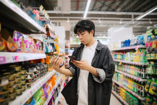 Student Looking At Smartphone While Choosing Items In Supermarket