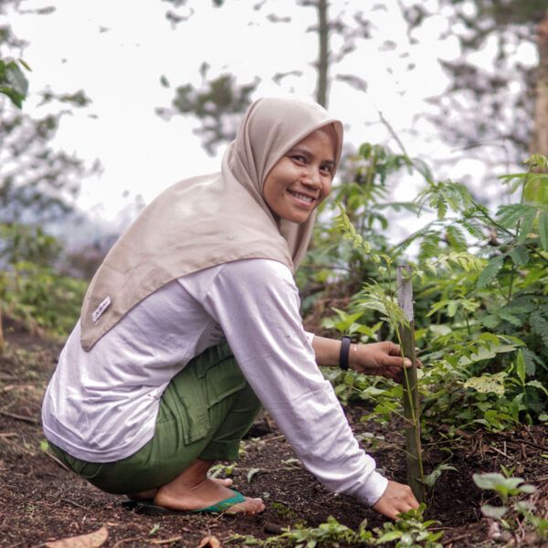woman smiles as she crouches next to coffee plant